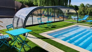 Une piscine avec un patio vitré, des chaises longues bleues et une table.