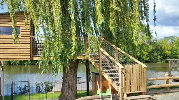 Une cabane en bois dotée d’un balcon, d’un escalier et offrant une vue sur un lac.