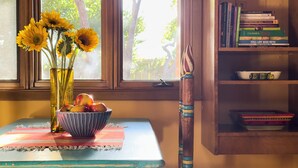 Ein Tisch mit einer Sonnenblumenvase, einer Apfelschale und einem Holzstuhl.