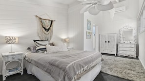 Une chambre à coucher comprenant un lit, des tables de chevet, une commode, un miroir et une décoration murale en macramé.