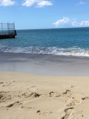 A beach with footprints in the sand, a metal fence, and calm ocean waves. - Beautiful gated spacious condo 5 minute walk to beach, restaurants and Hip Strip (Montego Bay)