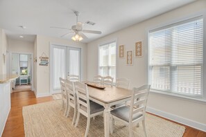 A dining area with a wooden table and chairs, a ceiling fan, and large windows with blinds.