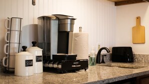 A kitchen counter with a coffee maker, sugar and coffee containers, a paper towel holder, a bottle of dish soap, a toaster, and a wooden cutting board on the wall. - Cozy and Clean Park City Studio (Park City)