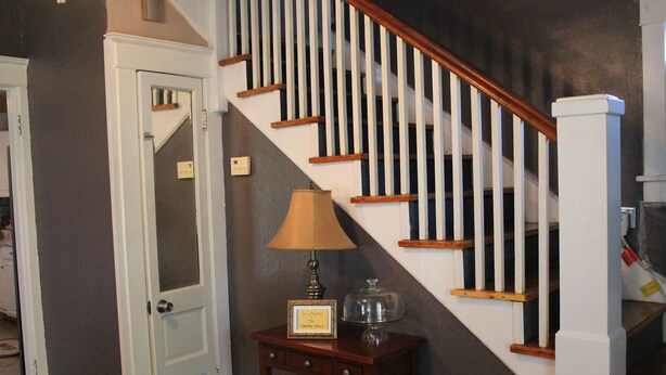 Un escalier avec des marches en bois et des balustrades blanches, une porte avec des panneaux de verre dépoli, et une petite table sur laquelle se trouvent une lampe et des objets décoratifs.