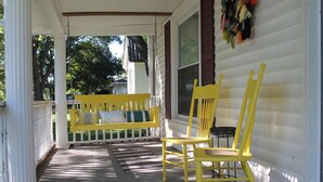 Une véranda avec un banc et des chaises jaunes, des colonnes blanches et une clôture blanche.