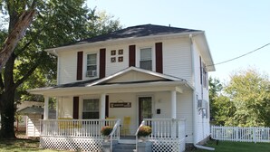 Une maison à deux étages avec un porche à l’avant, une enseigne indiquant « The Hamilton House » et une clôture blanche en piquets.