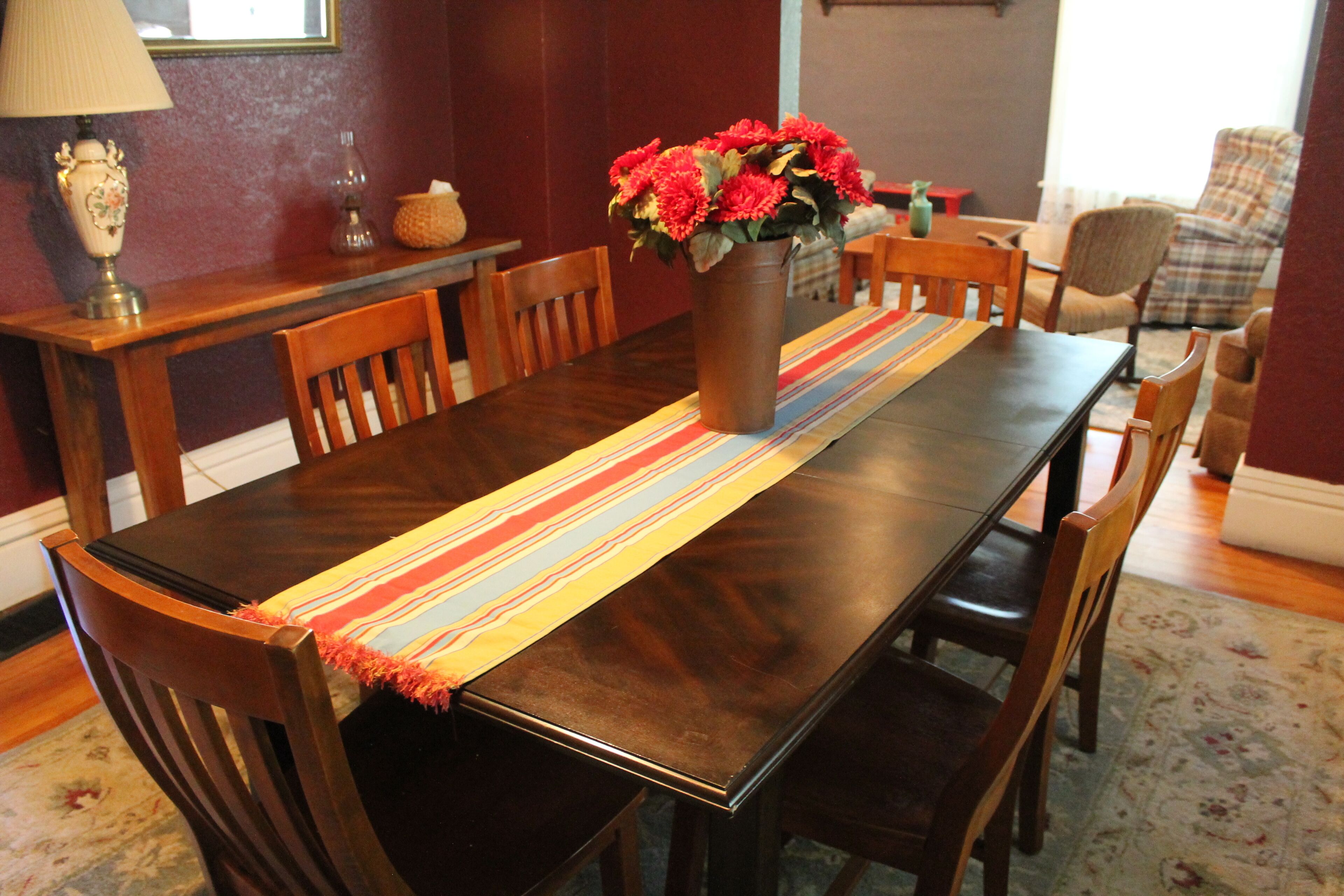 A dining table with a vase of flowers, wooden chairs, and a striped table runner.