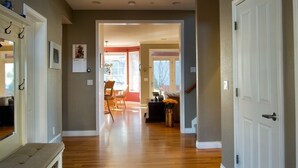 A hallway with wooden flooring, a dining area with chairs and a table, and a door leading to another room.
