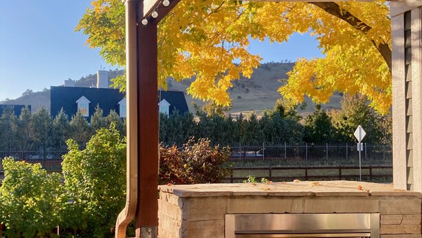 An outdoor patio with a stone fireplace, wooden chairs, and a pergola with string lights.