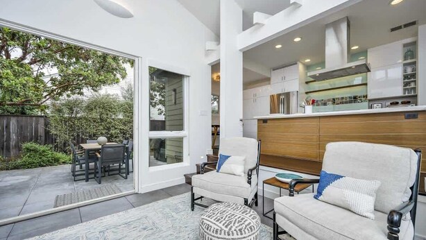 Un interior moderno con zona de comedor, dos sillones, un taburete estampado y una cocina con armarios blancos y encimera de madera.