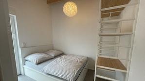 Un dormitorio con cama, dos almohadas, una lámpara colgante y una escalera metálica blanca.