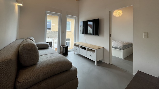 Una sala de estar moderna con un sofá, un televisor instalado en la pared y techo de madera.