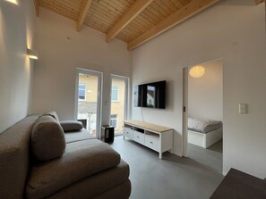 Ett modernt vardagsrum med en soffa, en tv som är monterad på väggen och ett träpanelat tak.