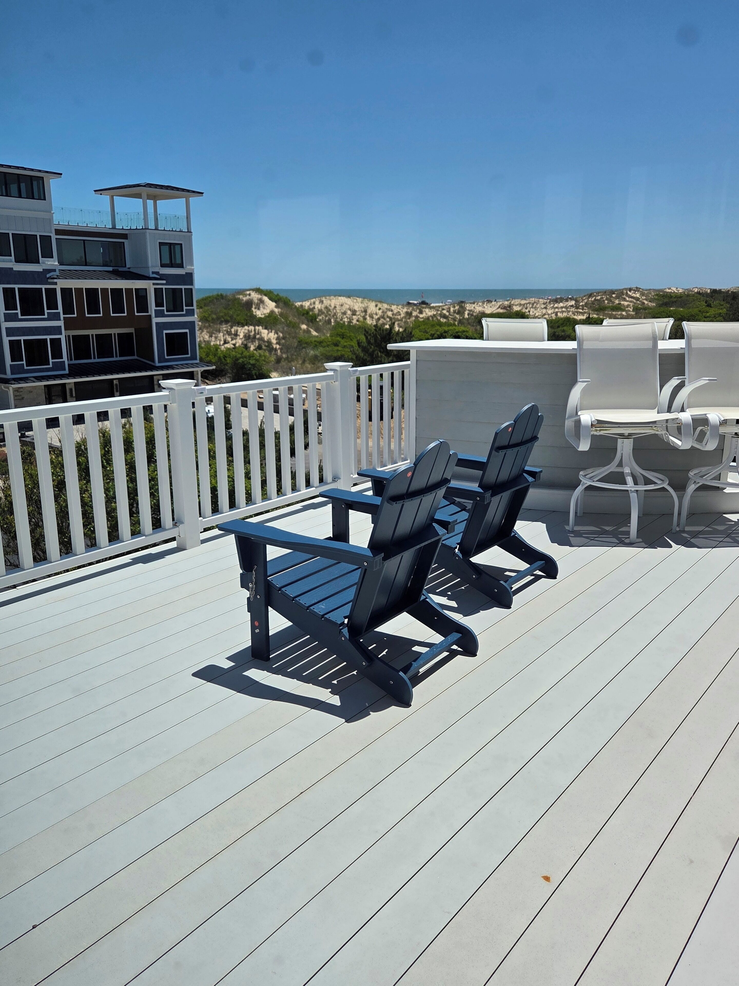 A deck with outdoor furniture, a white fence, and a view of the ocean.