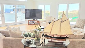 Una sala de estar con un ventanal grande, un ventilador de techo, un televisor de pantalla plana, un velero a escala y un sofá.