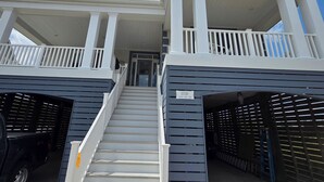 Un edificio de dos pisos con un balcón en el nivel superior, una escalera que conduce a la entrada y un garaje con un coche estacionado adentro.