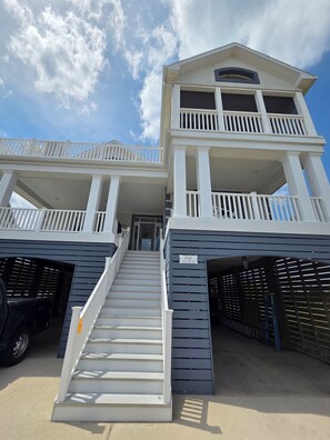 A two-story building with a balcony on the upper level, a staircase leading to the entrance, and a garage with a car parked inside. - Renovated Luxury Home w/Ocean & Bay Views in Gated Community (Fenwick Island)