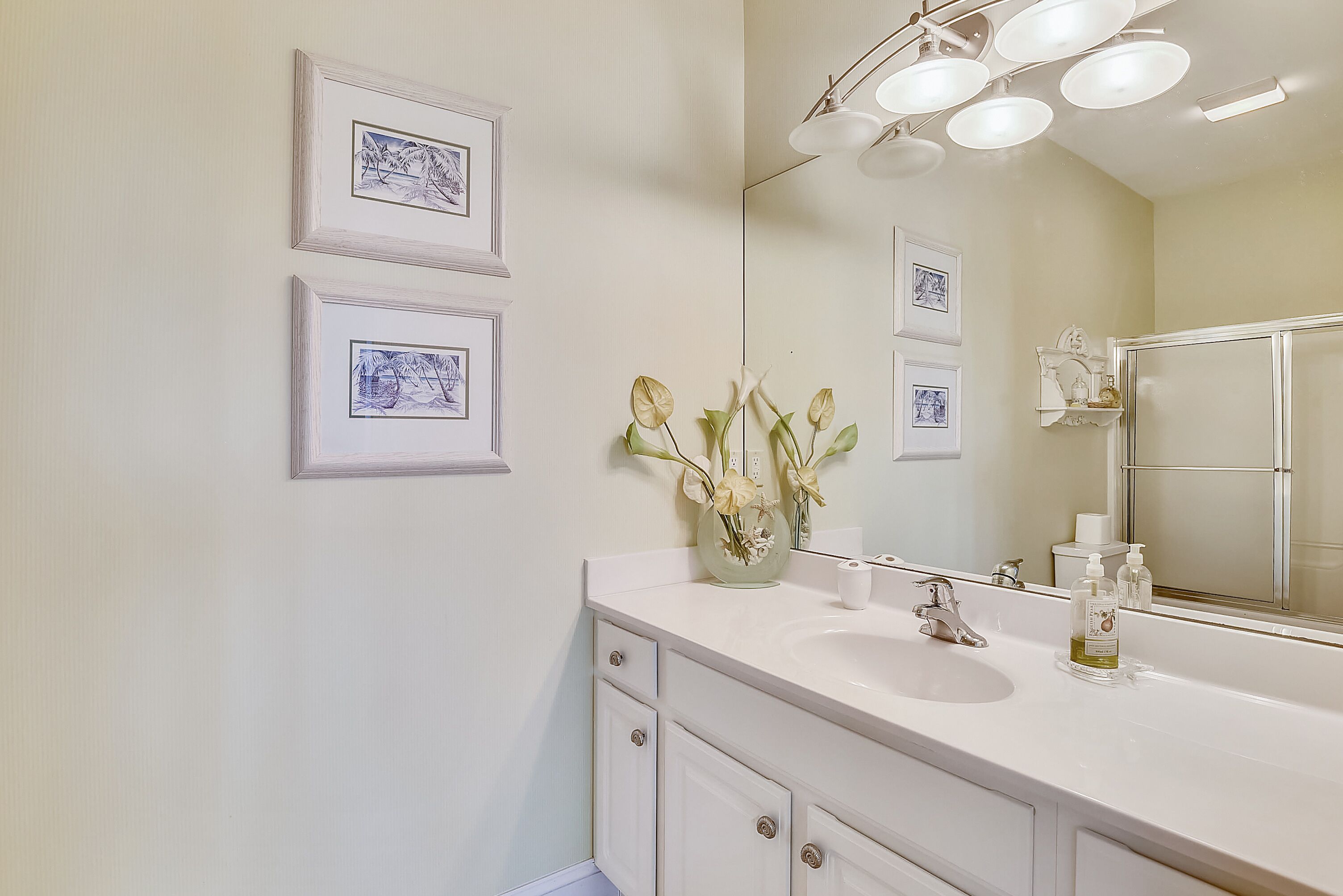 A bathroom with a white sink, a mirror, and framed pictures on the wall.