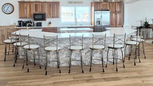 Una cocina amplia con una isla grande, taburetes de bar, armarios de madera e iluminación colgante.