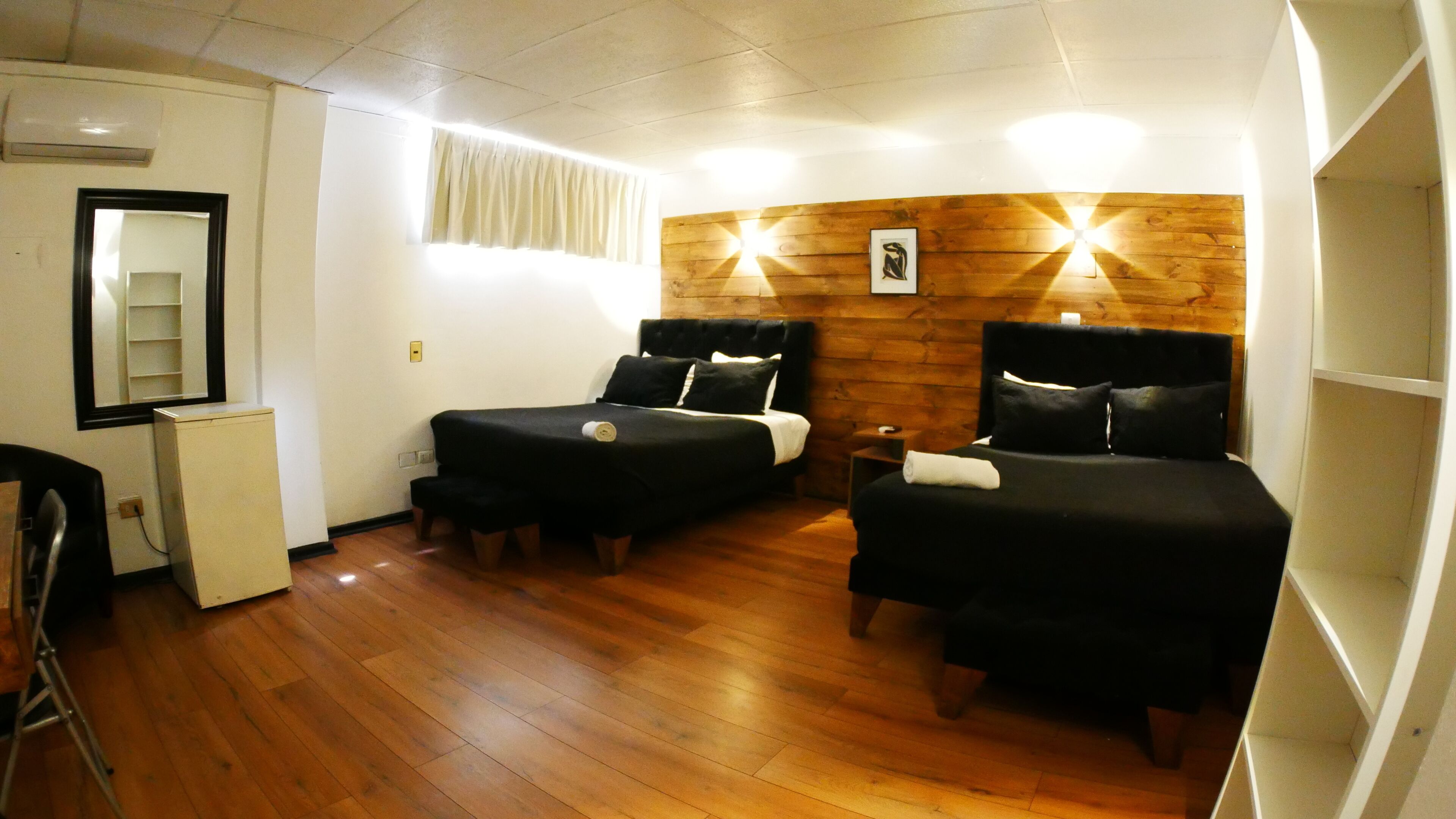 A room with two beds, a desk, a chair, a mirror, and a wooden wall.