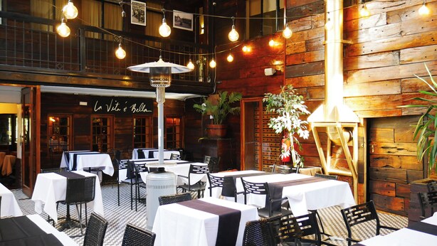 An indoor dining area with tables and chairs, wooden walls, and hanging light bulbs. - Hotel Sonetto (Santiago)