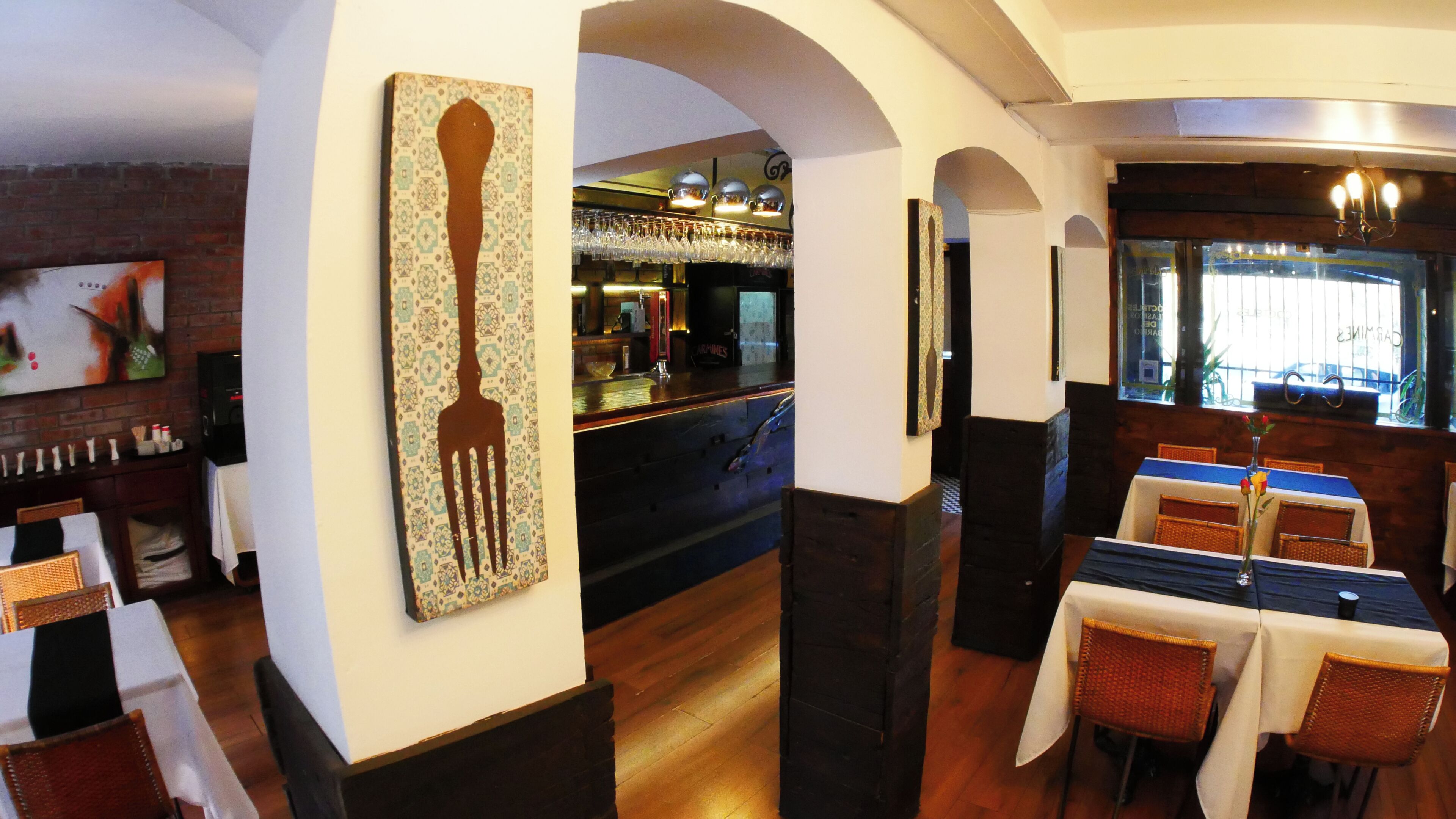 A restaurant interior with a bar area, tables with chairs, and a patterned wall decoration.