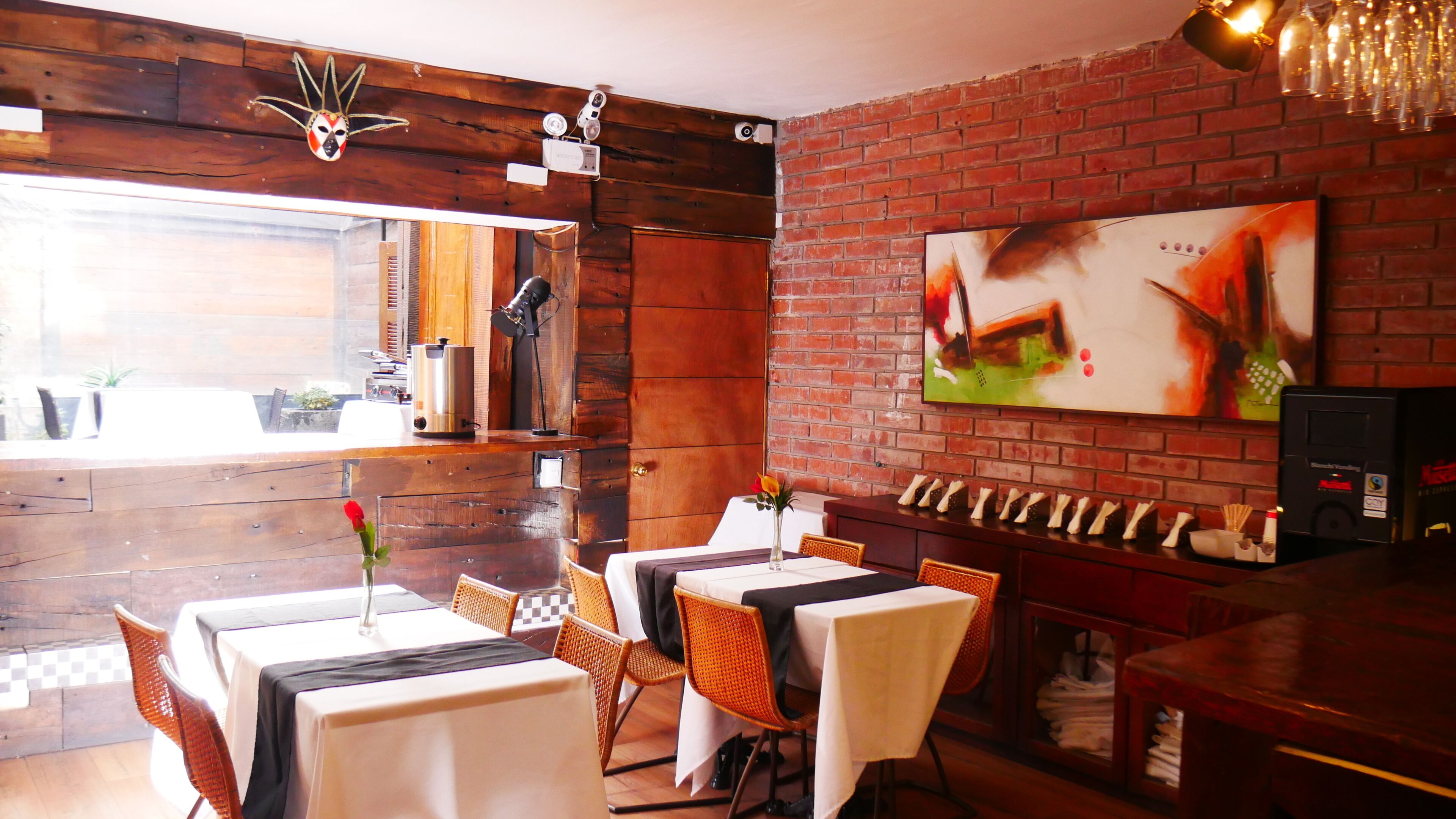 A restaurant with wooden walls, a brick wall, and a painting. Tables are set with white tablecloths and chairs.
