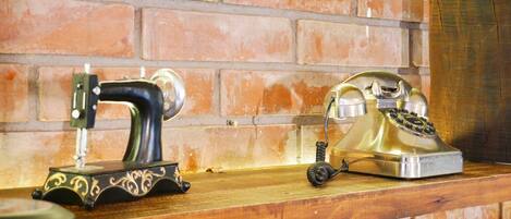 A sewing machine and an old-fashioned rotary phone on a wooden shelf against a brick wall.
