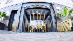 A building entrance with a large metal gate, a stone facade, and a palm tree to the left. - Hotel Sonetto (Santiago)