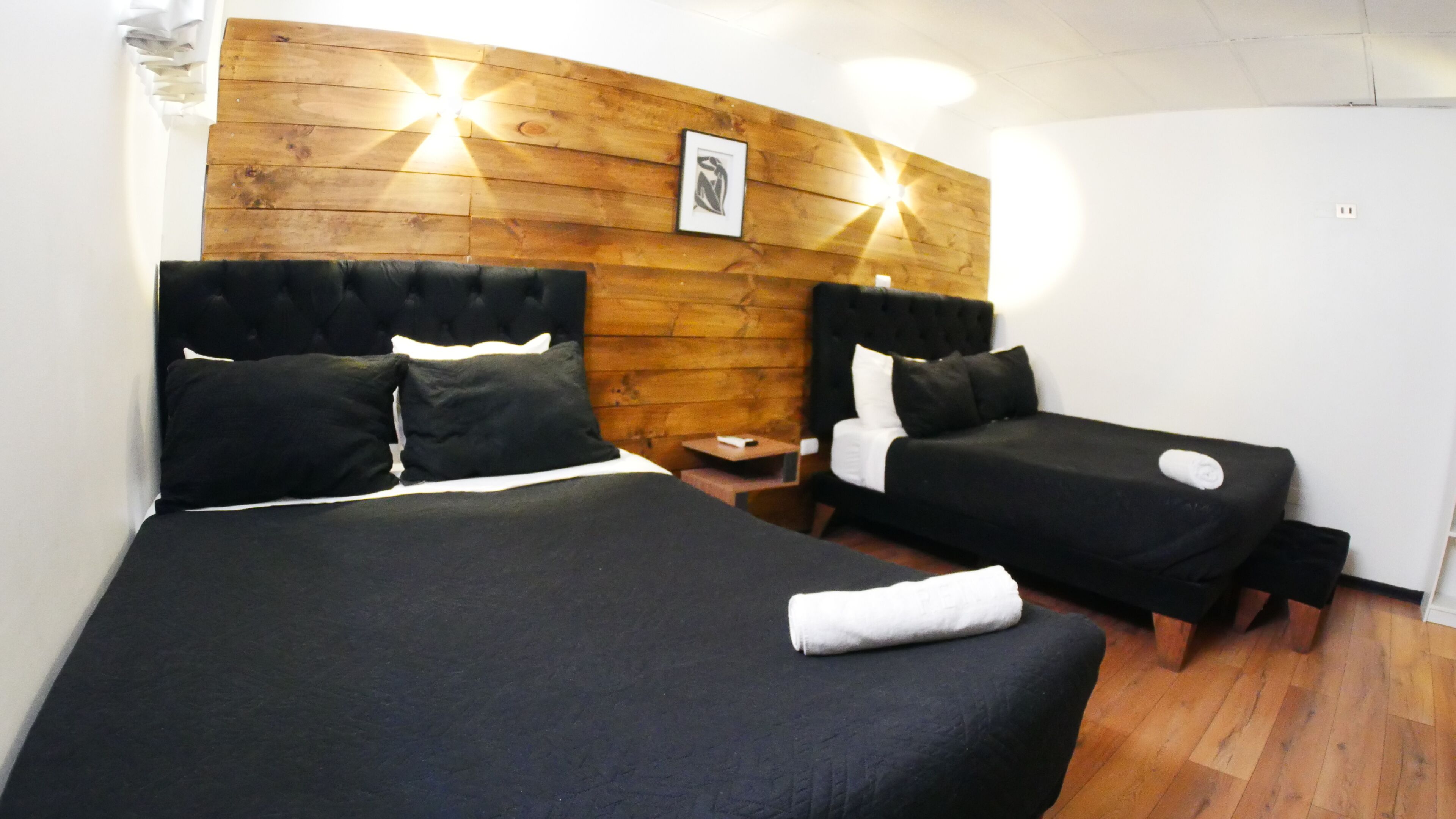 A hotel room with two beds, a wooden headboard, a small bedside table, and a framed picture on the wall.