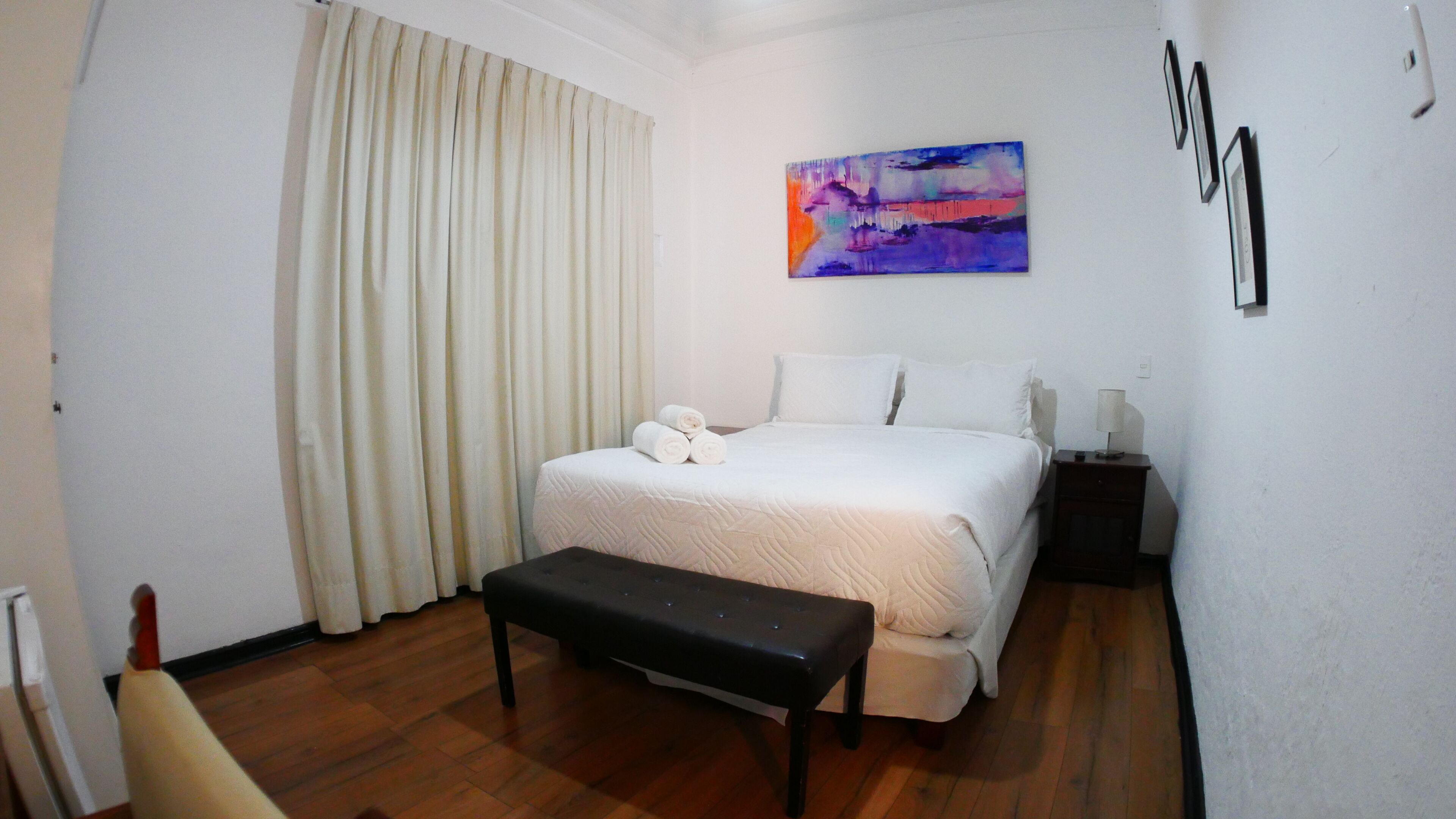 A hotel room with a bed, a bench, a painting, and a nightstand.