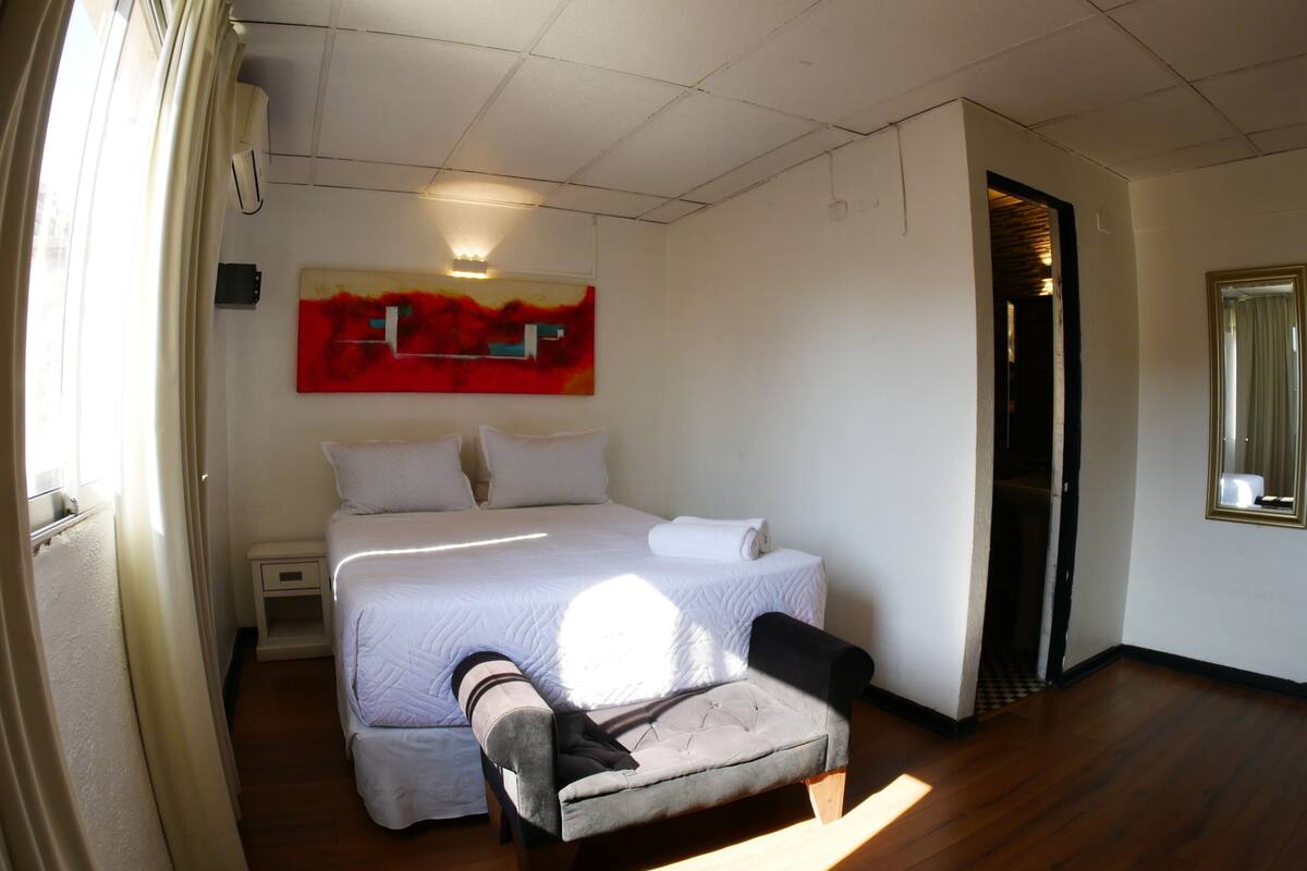 A hotel room with a bed, a chair, a painting, and a mirror.