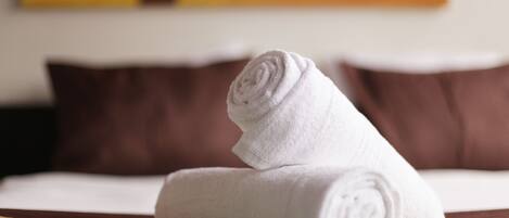 A neatly folded white towel on a bed with brown pillows.