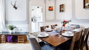 Un comedor con una mesa de madera dispuesta para cuatro, platos blancos y un jarrón con flores.