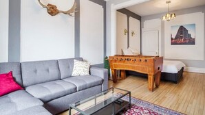 Una sala de estar moderna con un sofá gris, una mesa de futbolín y una mesa de centro de vidrio.