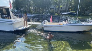 A marina with boats docked, clear water, and a dock with a person standing and another in the water.
