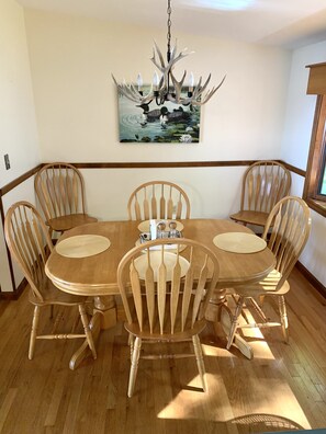 Un comedor con una mesa y sillas de madera, una araña y un cuadro en la pared.
