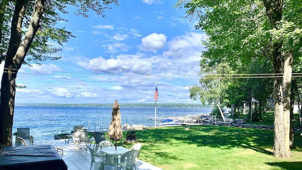 A deck with outdoor seating overlooking a body of water, a flag, and a grassy area.