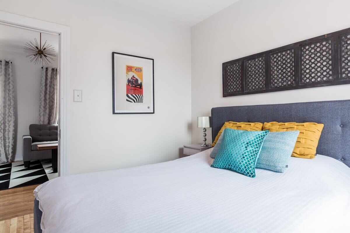 Une chambre d’hôtel avec un lit, une table de chevet, une lampe, un tableau encadré et un panneau décoratif au mur.