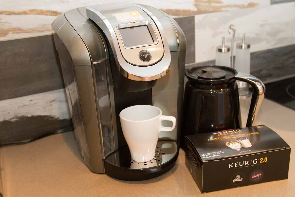 Eine Keurig 2.0 Kaffeemaschine mit weißer Tasse und Kaffeekanne auf einer Arbeitsplatte.