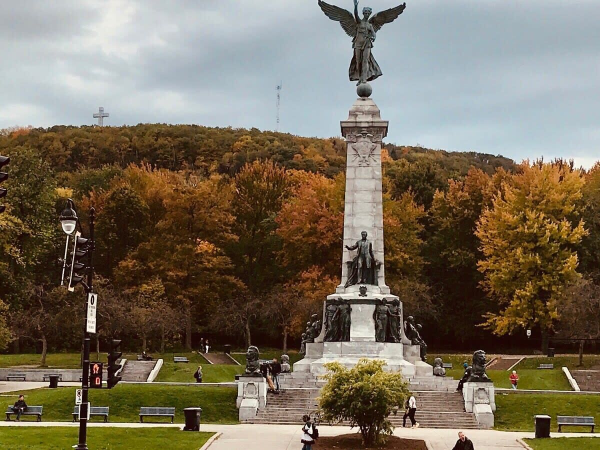 Ett monument med en staty högst upp, omgivet av en park med bänkar och träd.