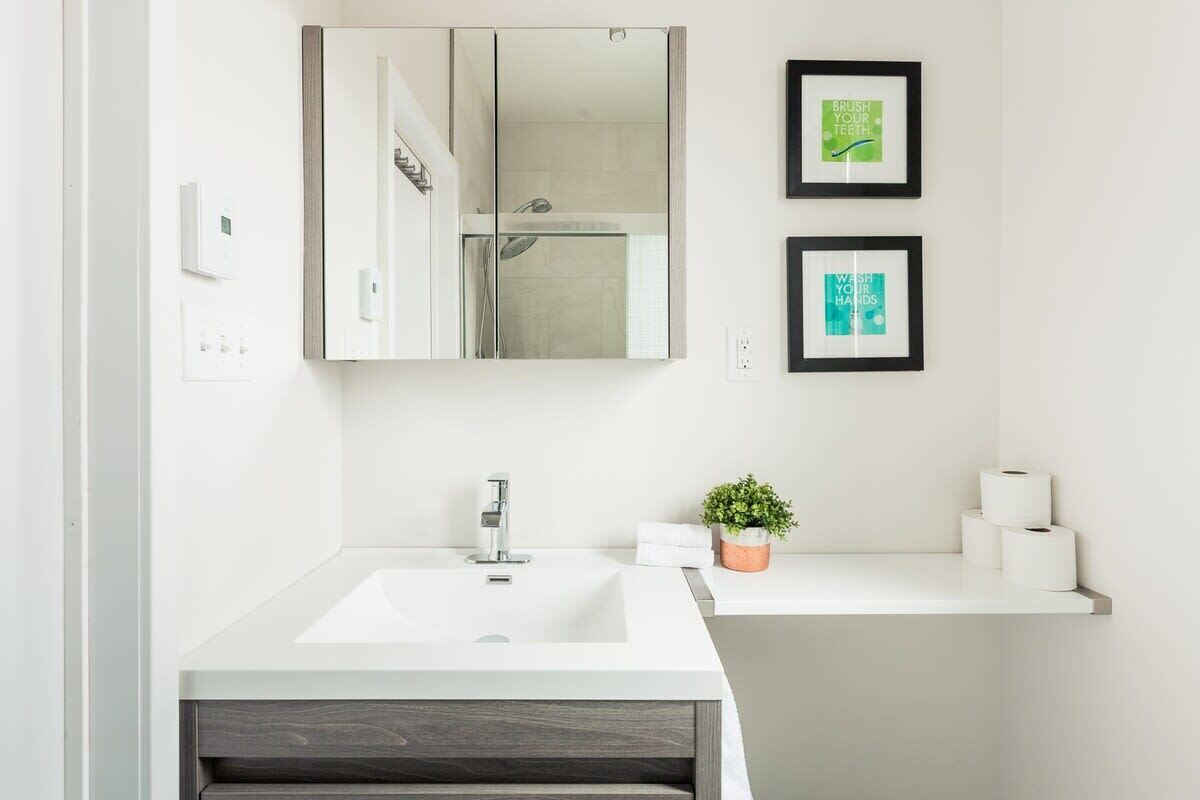 A modern bathroom with a large mirror, a white sink, and two framed motivational posters.