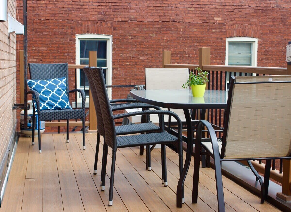 Eine Terrasse mit rundem Tisch und Stühlen, einem Blumentopf und einer Ziegelwand.