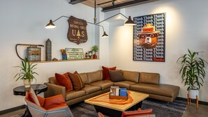 A modern living room with a brown leather sofa, two armchairs, a coffee table, and decorative items including a sign about Sawtooth National Forest and a wall art featuring a bear. - The Wren (Missoula)