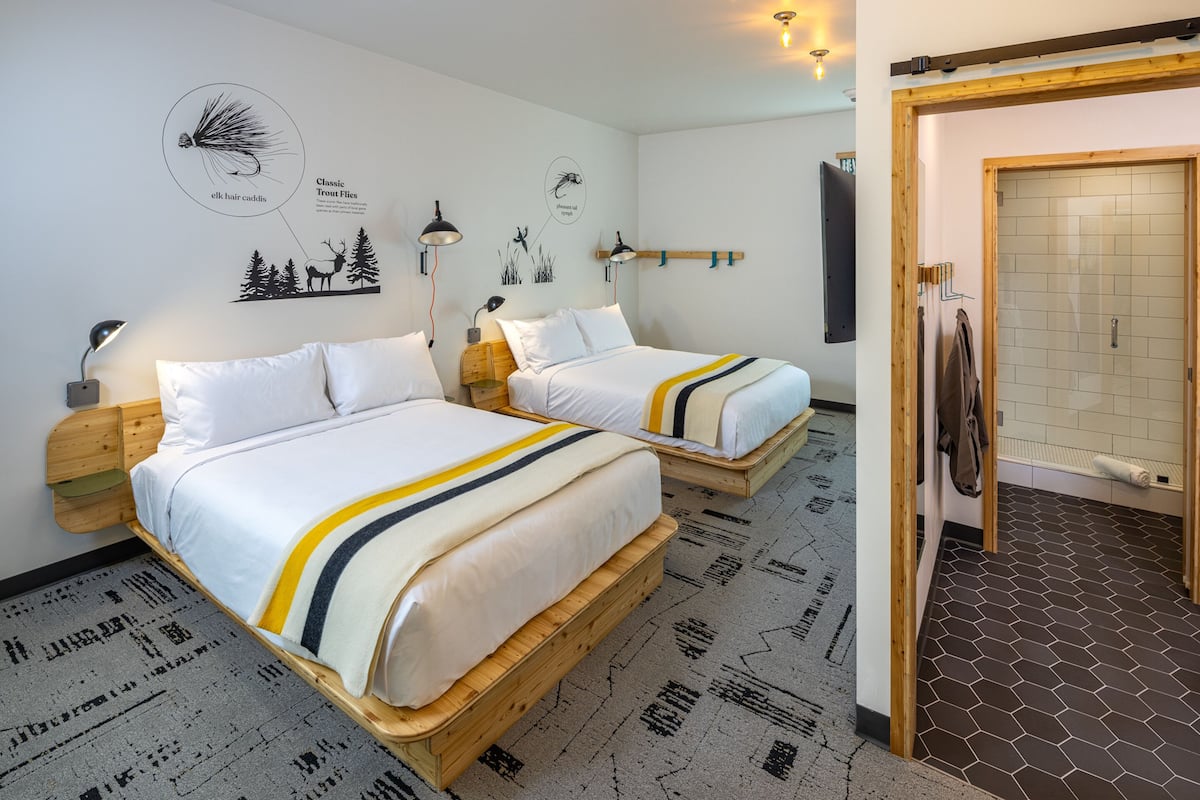 A hotel room with two wooden beds, a wall-mounted coat rack, and a shower area.
