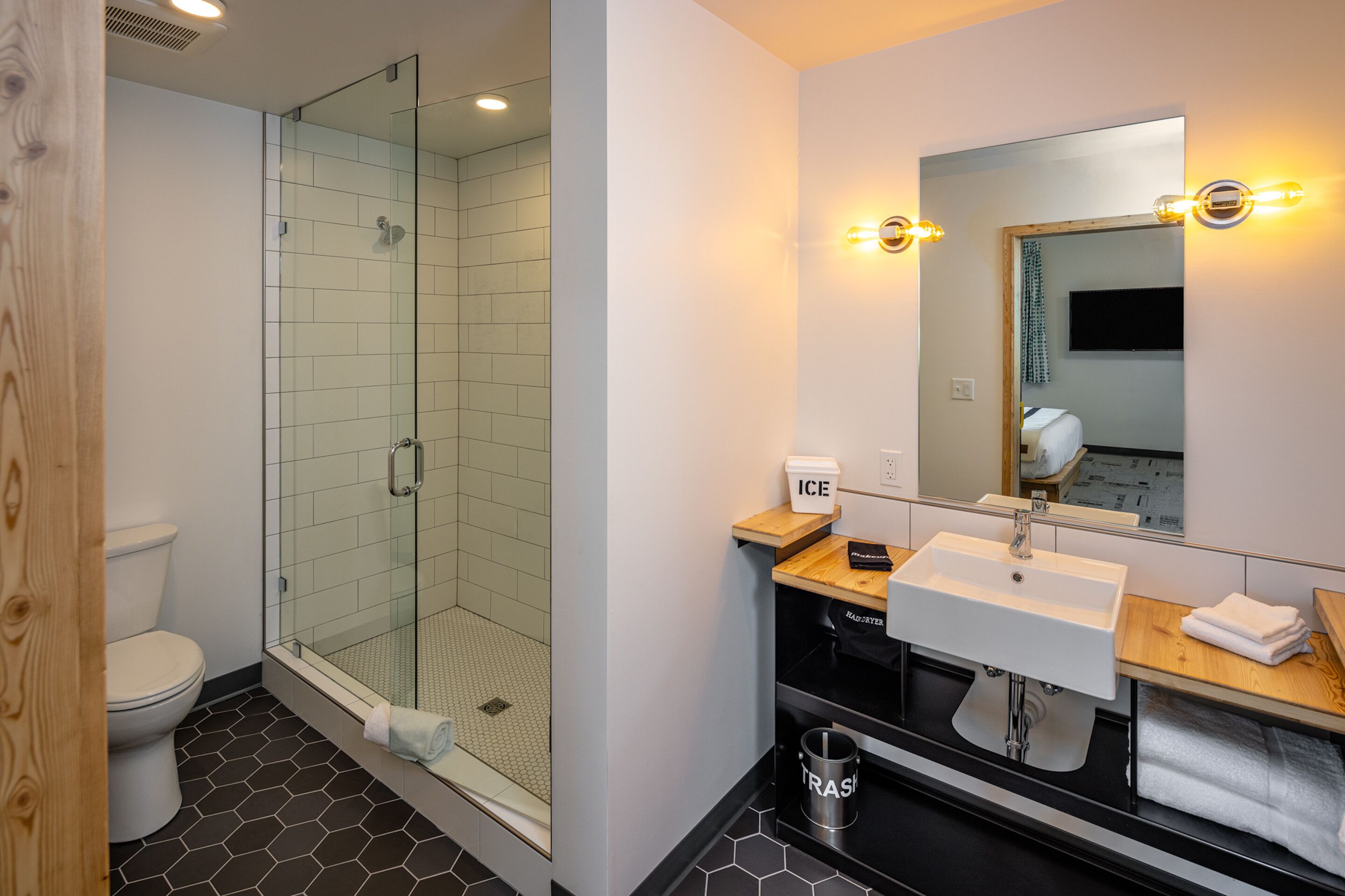 A modern bathroom with a glass-enclosed shower, a white sink, and a mirror with lights.