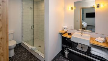 A modern bathroom with a glass-enclosed shower, a white sink, and a mirror with lights.