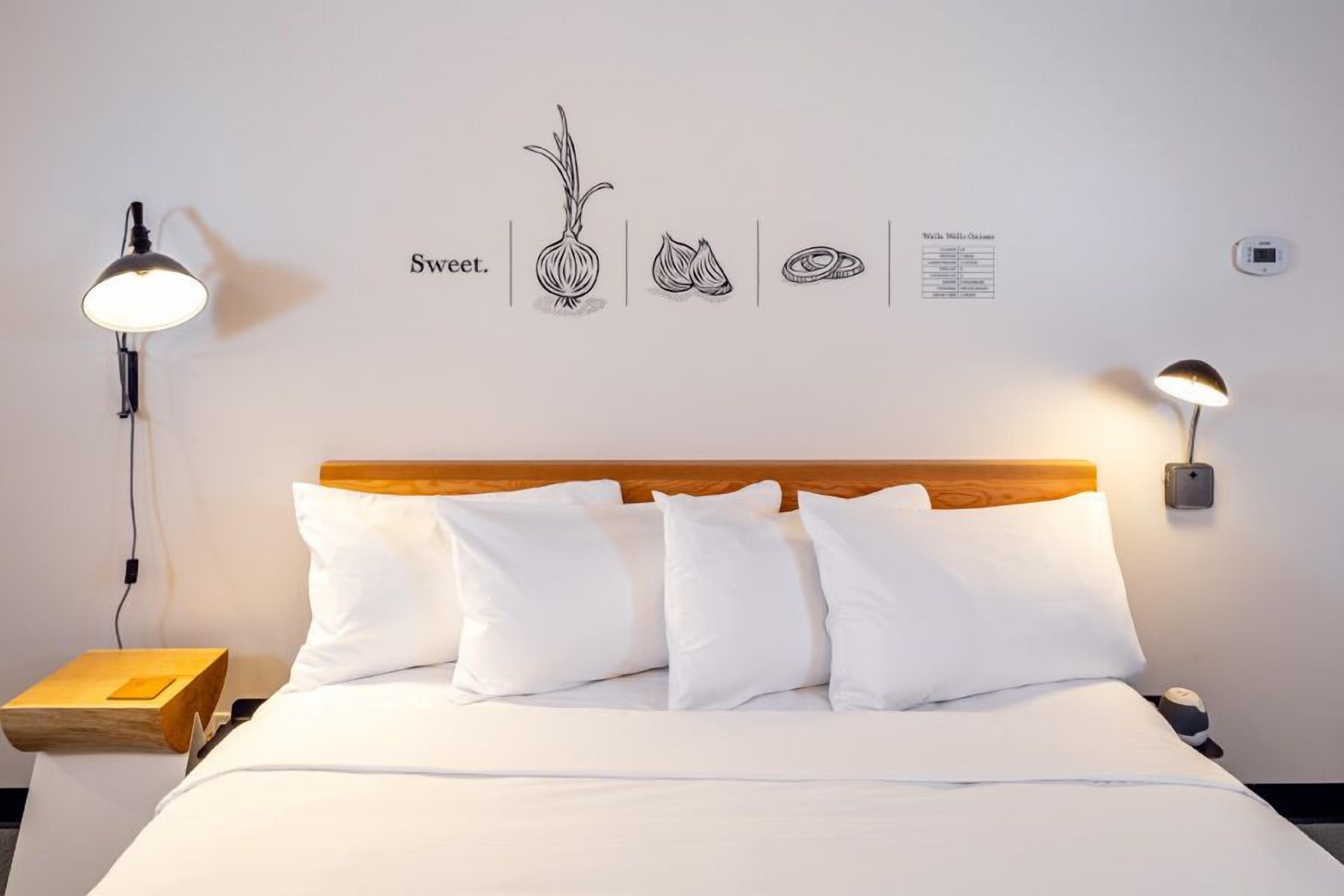 A neatly made bed with white bedding and pillows, a wooden headboard, and two wall-mounted lamps.