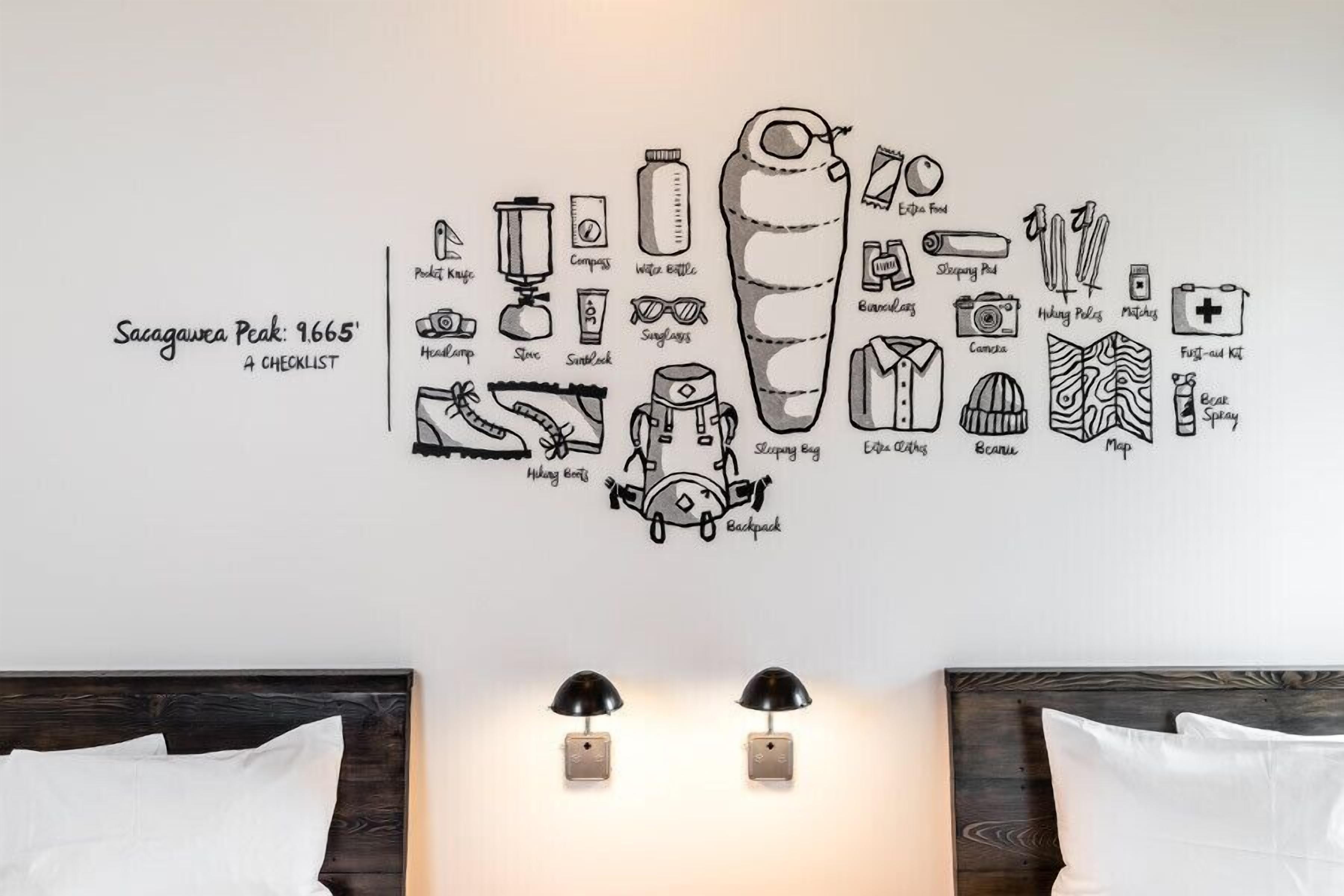 A room with a wall-mounted checklist of hiking and camping gear, two bedside lamps, and a neatly made bed.