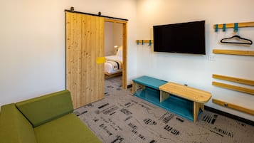Quarto moderno com sofá verde, um banco de madeira, TV fixada na parede e porta deslizante que dá para uma cama.